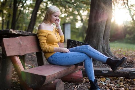 Jeune Femme Blonde S asseyant Sur Un Banc En Bois En Parc écoutant La Musique Photo stock