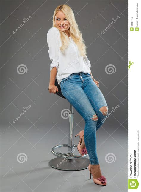 Fille Blonde S Asseyant Sur Les Jeans De Port De Chaise Et La Chemise Blanche Image Stock