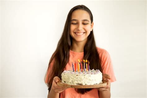 Retrato de alegre jovencita latina sonríe y sopla una vela en el pastel de cumpleaños agitando