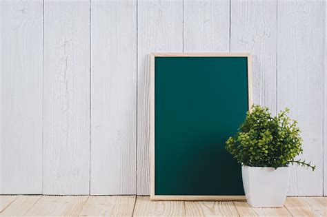 Blank Green Chalkborad With Wood Frame And Little Decorative Tree In White Vase On Wooden Table