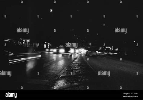 A Monochrome Image Of Cars Driving Down A Dimly Lit Street At Night