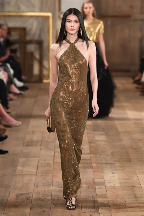 A Model Walks Down The Runway In A Gold Dress With Sequins On It