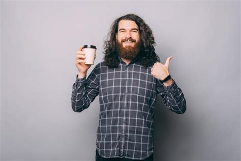 Hombre joven con barba sosteniendo un café para llevar sobre fondo gris