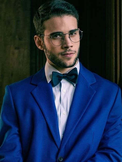 A Man In A Blue Suit And Bow Tie Standing Next To A Wooden Wall Wearing