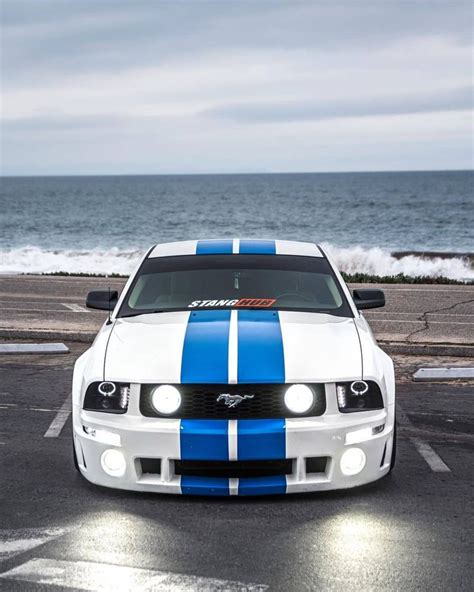 A White And Blue Mustang Parked In Front Of The Ocean