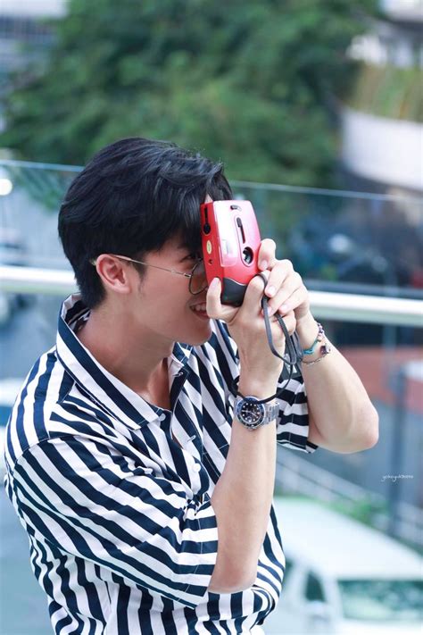 A Man In Striped Shirt Holding A Cell Phone Up To His Face