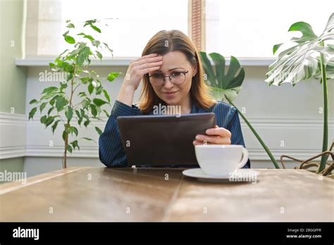 Smiling Mature Woman Having Breakfast At Home In Pajamas With Cup Of Tea Sitting At Table