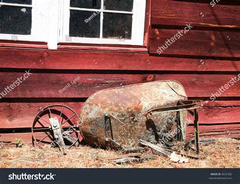 Old Rusty Antique Wheelbarrow Broken And Leaning Against Red Shed Stock