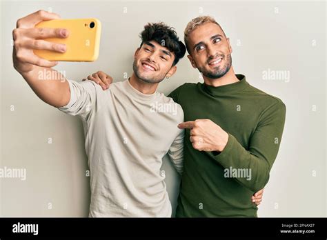 Homosexual Gay Couple Standing Together Taking A Selfie Photo With Smartphone Pointing Finger To