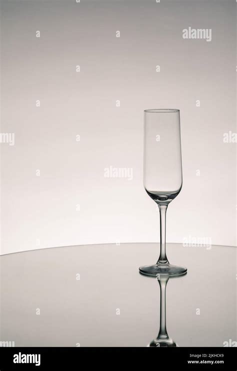 A Grayscale Shot Of An Empty Glass Cup With Reflection On A Mirror