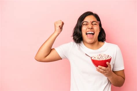 Mujer latina joven con cereales aislados sobre fondo rosa levantando el puño después de una