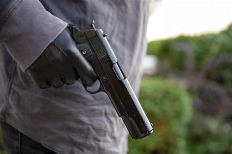 Premium Photo Gloved Hand Holding A Pistol Blur Nature Background