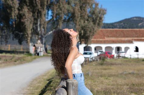 Curly Haired Brunette Spanish Woman Resting On The Fence Of The Path Leading To The Meadow