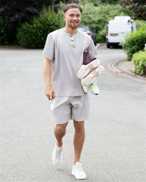 A Man Is Walking Down The Street With His Shoes In Hand And Smiling At