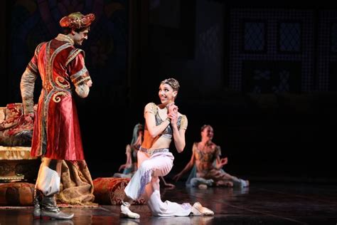 A Man And Woman In Costume On Stage With Other People Sitting Around