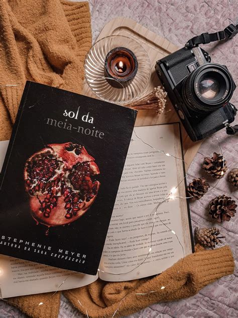 An Open Book Sitting On Top Of A Bed Next To A Camera And Some Pine Cones