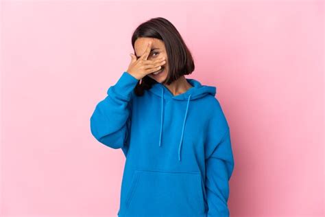 Jovem latina isolada em uma parede rosa cobrindo os olhos pelas mãos e sorrindo Foto Premium