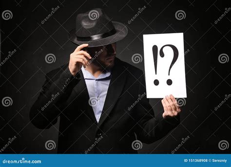 Detective Holding Sheet Of Paper With Exclamation And Interrogation Marks On Dark Background