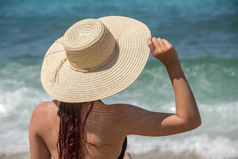 La Fille Du Dos Dans Le Chapeau S Assied Sur La Plage Photo Stock