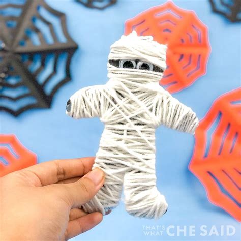 a hand holding a string wrapped toy in front of some spider webs on a blue background