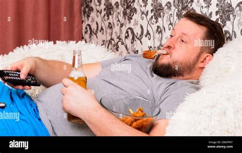 Bearded Fat Man With A Big Belly Lies On The Sofa With Fast Food