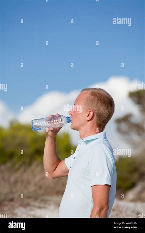 young man drinking water on the beach on a dune in summer Stock Photo - Alamy