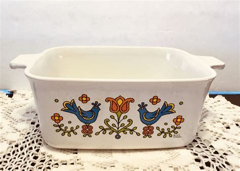 A White Casserole Sitting On Top Of A Doily With Flowers And Birds