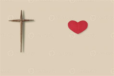 Wooden christian cross and red paper heart on light brown background
