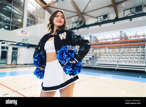 Medium Shot Of Brunette Short Haired Cheerleader In A Jacket Posing With Blue Shiny Pom Poms In