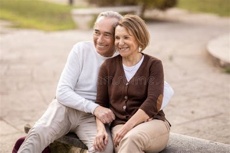 Loving Mature Couple Embracing Sitting On Bench In Park Outside Stock