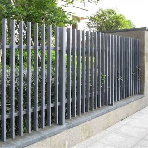 a tall metal fence sitting on the side of a road next to a tree and bushes