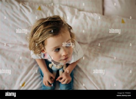 Young Blonde Girl Sat On Her Bed In Her Bedroom Looking With Toys Stock