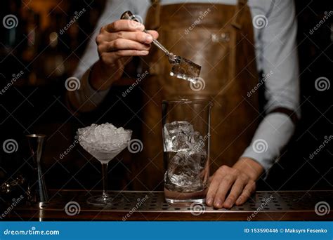 Male Bartender Putting A Big Ice Cube To The Measuring Glass Cup Stock