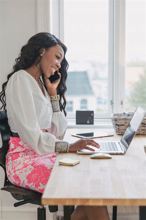 Black Woman In An Office Smiling While Talking On The Phone By Stocksy Contributor Lior