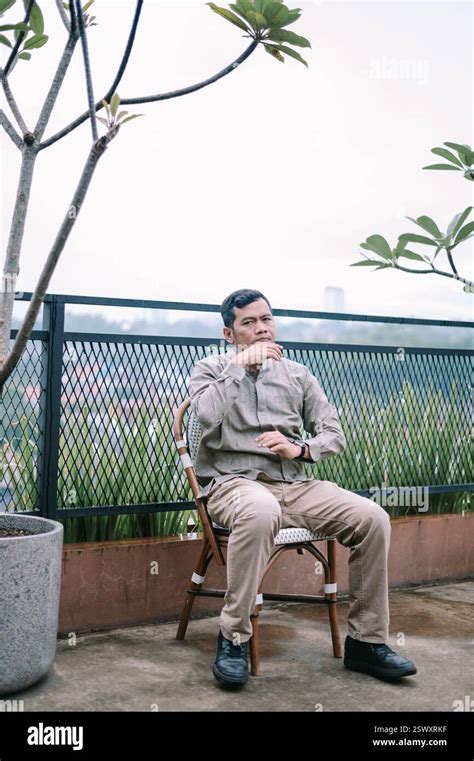 A Mature Man Sits Thoughtfully On A Rooftop Overlooking A Cityscape He Seems Pensive And