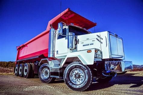 A Red And White Dump Truck Parked On The Side Of A Dirt Road In Front