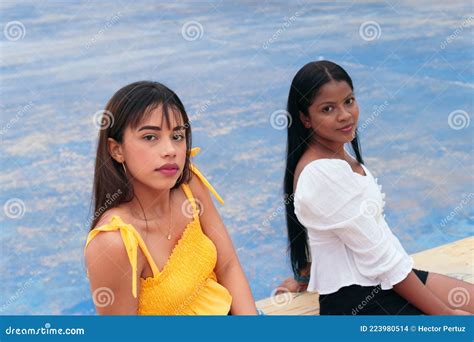 Two Latina Friends Sitting In The Park Looking At The Camera Stock