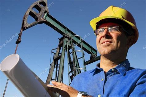 A Man In A Hard Hat And Glasses Is Standing Next To An Oil Pump