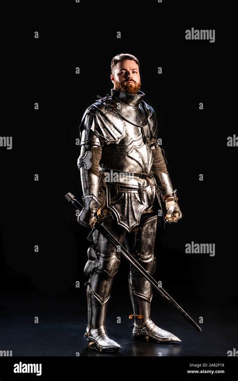 Handsome Knight In Armor Holding Sword Isolated On Black Stock Photo