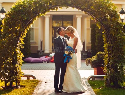 La Jeune Mariée Blonde Avec Un Bouquet Des Fleurs Dans Des Ses Mains Et Son Fiancé Se Tiennent