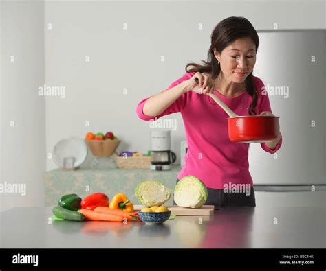 Mature Woman Cooking In Kitchen Looking At Contents Of Pot Stock Photo Alamy