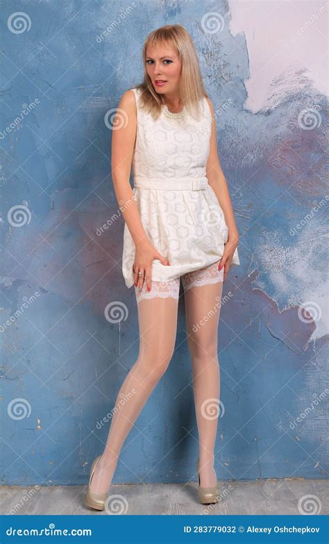 Long Legged Blonde Girl In Whi Minidress And White Stockings Posing At The Wall CartoonDealer