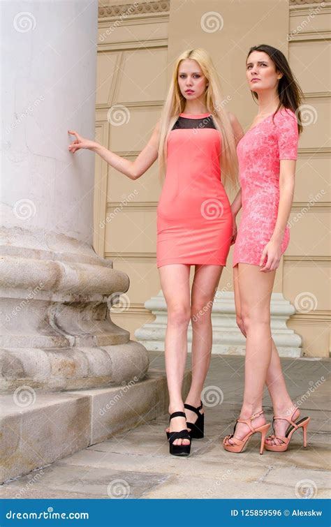 Las Muchachas Blonde Y Morenita En Vestidos Rosados Cortos Se Colocan En El Edificio De Piedra