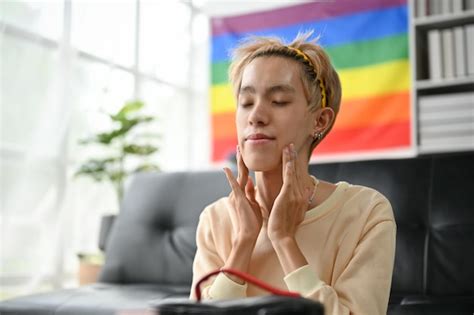 Un hombre gay asiático feliz está aplicando crema hidratante de tratamiento facial y masajeando