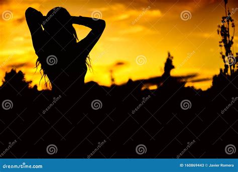 Silhouette Of A Woman Standing With Her Arms Raised Up At Sunset Stock