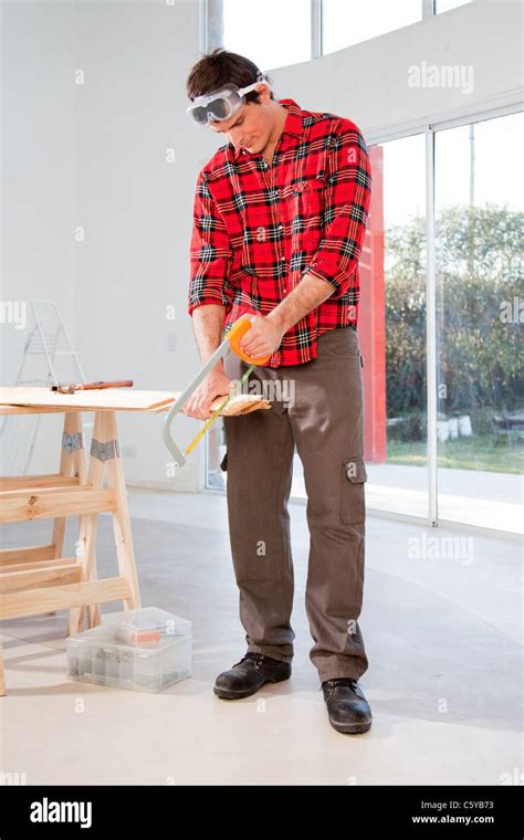 A carpenter cutting wood with a hand saw in a house Stock Photo - Alamy