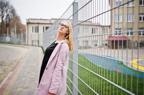 Fille Blonde à Lunettes Et Manteau Rose Tunique Noire Et Sac à Main Posés Contre La Clôture à La