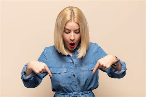 Premium Photo Blonde Woman With Open Mouth Pointing Downwards With Both Hands Looking Shocked