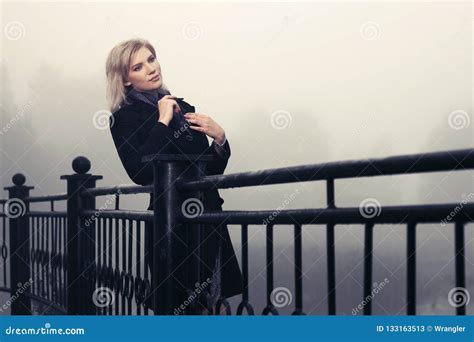 Young Fashion Woman In Black Coat Leaning On Railing Outdoors Stock