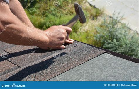 Roofer With Hammer In Motion Laying Asphalt Shingles Tiles On House